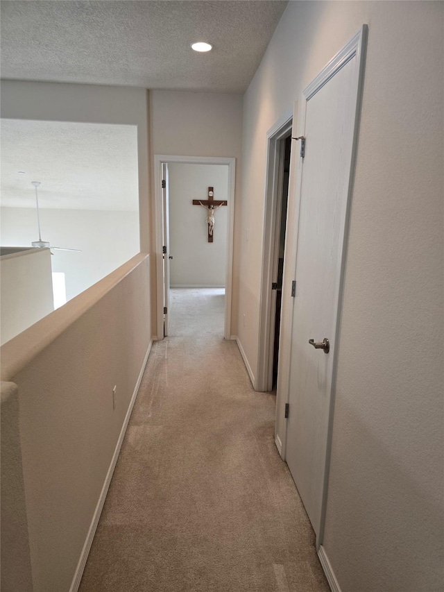 hallway with a textured ceiling and light carpet