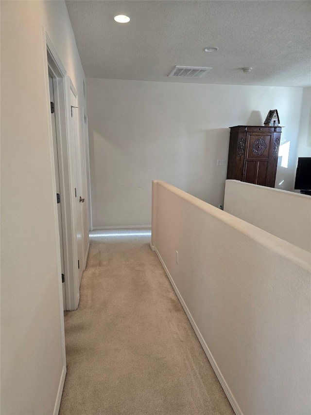 hallway featuring a textured ceiling and light carpet