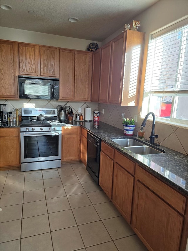 kitchen featuring sink, dark stone counters, a textured ceiling, light tile patterned flooring, and black appliances