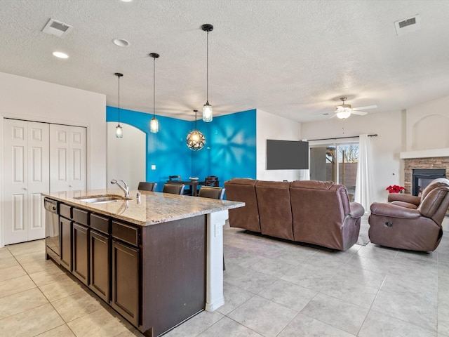 kitchen with pendant lighting, a center island with sink, sink, dark brown cabinets, and light stone counters