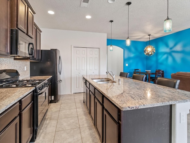 kitchen featuring black appliances, sink, hanging light fixtures, an island with sink, and dark brown cabinets