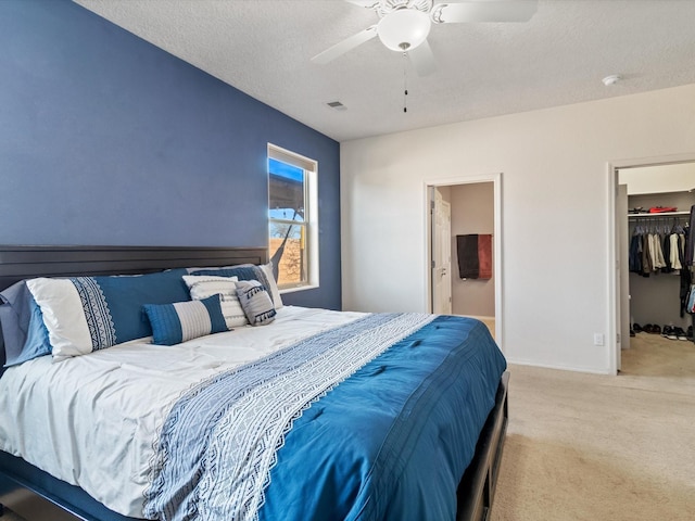 bedroom with ceiling fan, a spacious closet, a textured ceiling, light carpet, and a closet