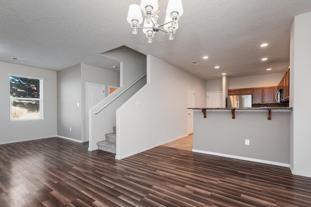 unfurnished living room featuring a chandelier, a textured ceiling, and dark wood-type flooring