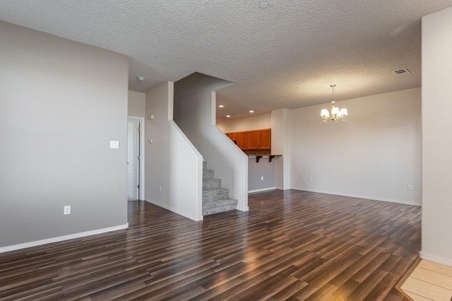 unfurnished living room featuring a chandelier, a textured ceiling, and dark wood-type flooring