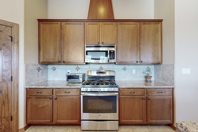 kitchen featuring light tile patterned flooring, stainless steel appliances, decorative backsplash, and light stone countertops