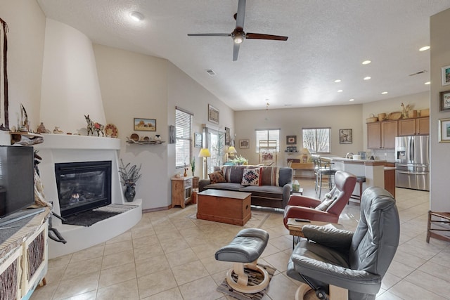 living room with ceiling fan, a textured ceiling, light tile patterned floors, and a large fireplace