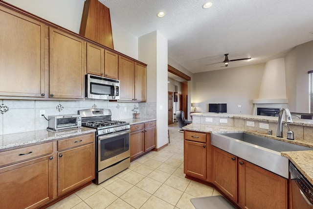 kitchen featuring ceiling fan, sink, stainless steel appliances, a textured ceiling, and light stone counters