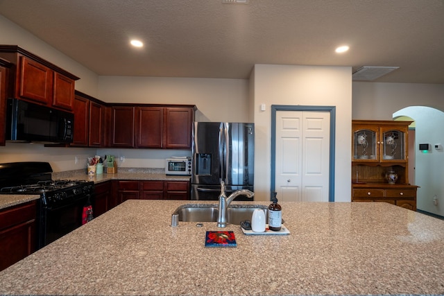 kitchen featuring a kitchen island with sink, sink, light stone counters, and black appliances