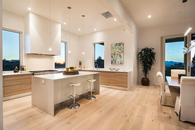 kitchen featuring a kitchen island, decorative light fixtures, stainless steel gas stovetop, a breakfast bar area, and light hardwood / wood-style flooring