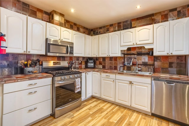 kitchen featuring appliances with stainless steel finishes, sink, white cabinets, light hardwood / wood-style floors, and tile counters