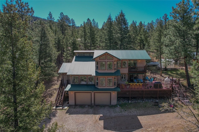 rear view of property with stairway, metal roof, gravel driveway, a forest view, and a garage