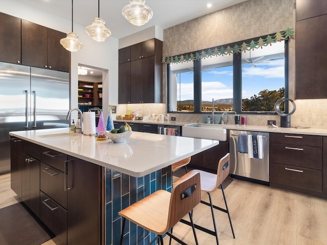 kitchen with a kitchen breakfast bar, dark brown cabinetry, stainless steel appliances, and a center island with sink