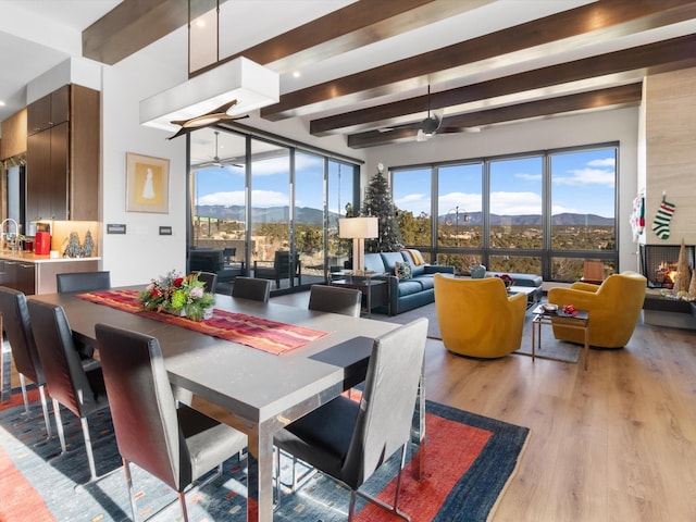 dining area with a mountain view, beamed ceiling, ceiling fan, and light wood-type flooring