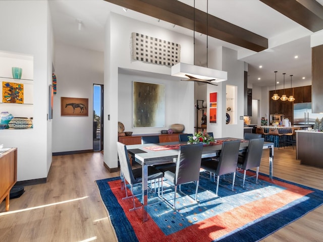 dining space with beamed ceiling, light hardwood / wood-style floors, a high ceiling, and a notable chandelier