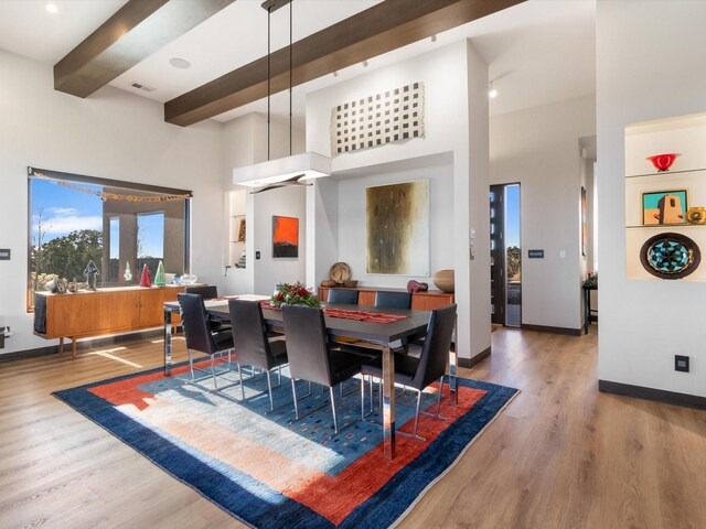 dining area featuring beam ceiling, wood-type flooring, and a towering ceiling