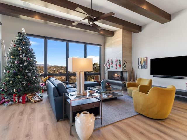 living room with beam ceiling, ceiling fan, a fireplace, and light wood-type flooring