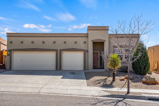 pueblo-style house with a garage, concrete driveway, and stucco siding