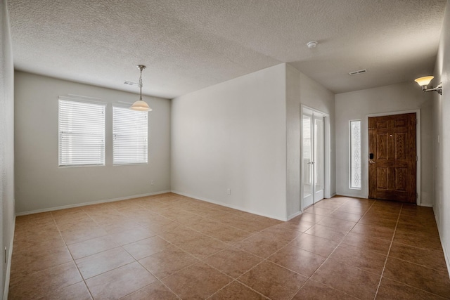 spare room with tile patterned flooring, visible vents, baseboards, and a textured ceiling