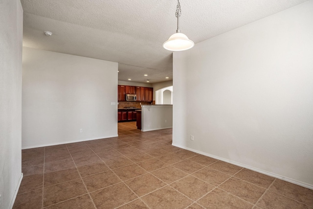 tiled empty room featuring arched walkways, recessed lighting, a textured ceiling, and baseboards