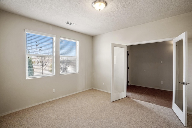 unfurnished bedroom with tile patterned flooring, visible vents, carpet, french doors, and a textured ceiling