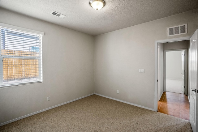 spare room with a textured ceiling, visible vents, carpet, and tile patterned flooring