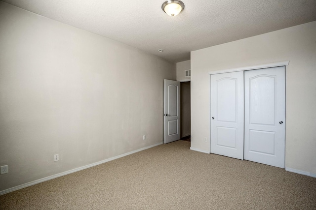 unfurnished bedroom with a closet, light colored carpet, a textured ceiling, and baseboards