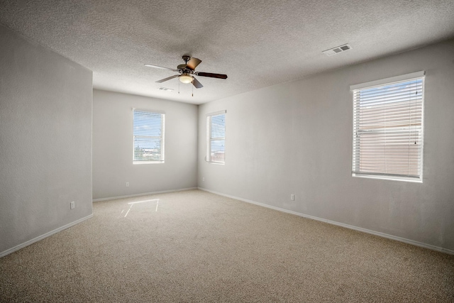 carpeted spare room with a textured ceiling, baseboards, visible vents, and ceiling fan