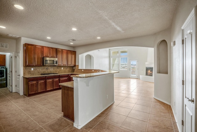 kitchen featuring stainless steel microwave, a large fireplace, decorative backsplash, arched walkways, and gas cooktop