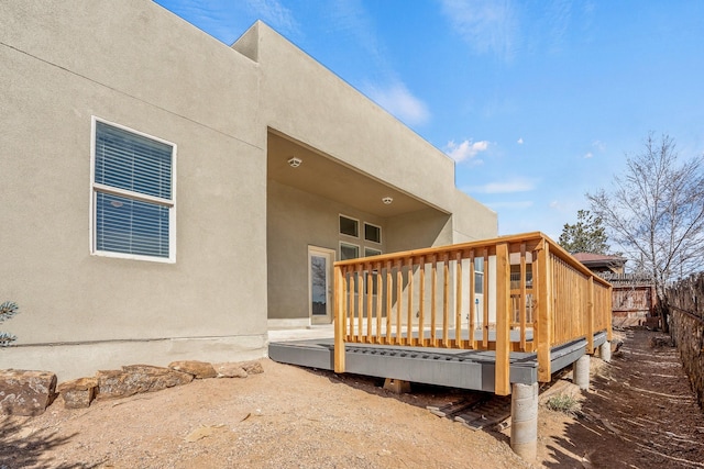 view of property exterior featuring stucco siding, a wooden deck, and fence