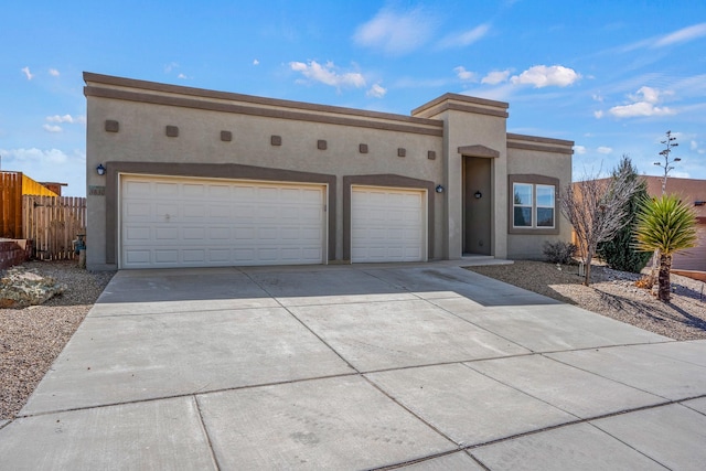 pueblo-style home with fence, a garage, driveway, and stucco siding