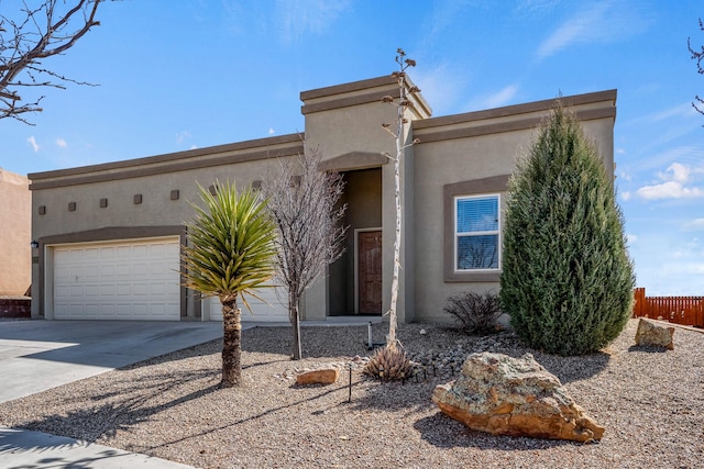 pueblo-style house with stucco siding, an attached garage, driveway, and fence