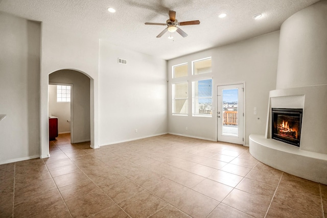 unfurnished living room featuring light tile patterned floors, visible vents, arched walkways, ceiling fan, and a glass covered fireplace