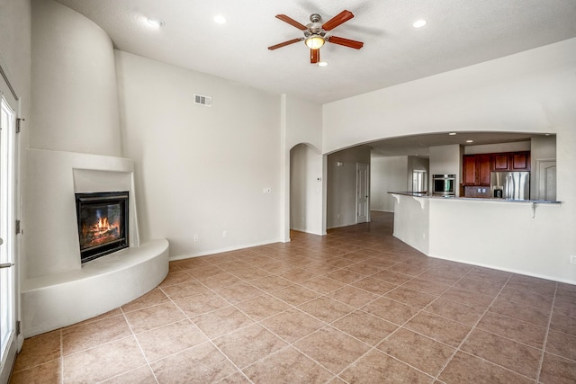 unfurnished living room featuring visible vents, recessed lighting, arched walkways, a fireplace, and ceiling fan