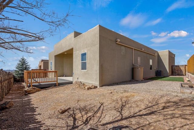 view of side of home with central air condition unit, stucco siding, a wooden deck, and a fenced backyard