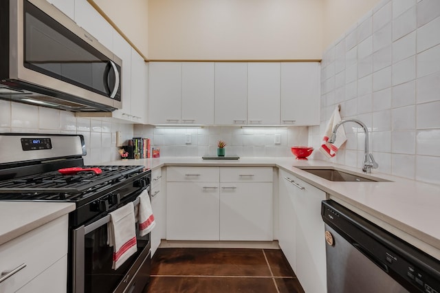 kitchen featuring sink, tasteful backsplash, dark tile patterned floors, white cabinets, and appliances with stainless steel finishes