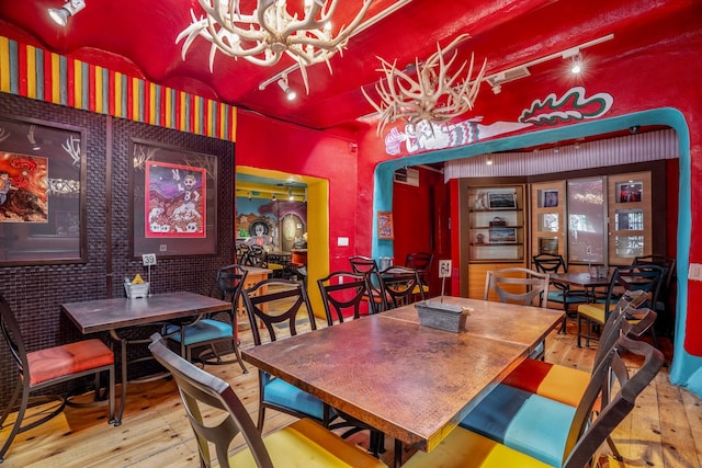 dining area with a chandelier, wood-type flooring, and brick wall