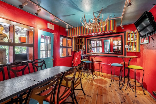 dining space featuring hardwood / wood-style floors, a textured ceiling, track lighting, and bar