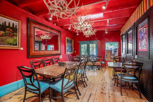 dining space with beam ceiling, french doors, rail lighting, a notable chandelier, and hardwood / wood-style floors