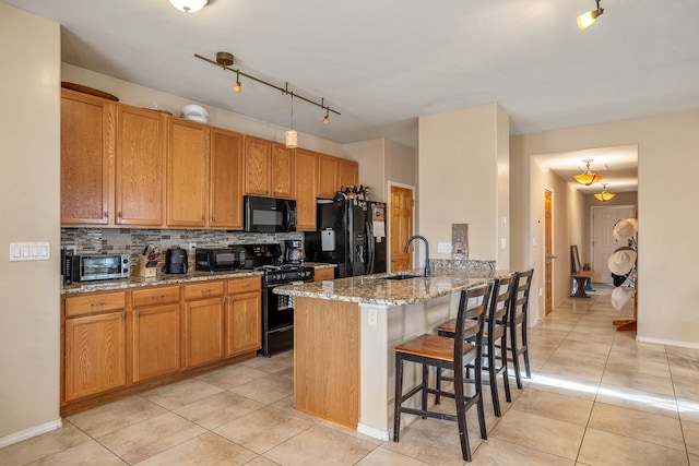 kitchen featuring black appliances, light stone counters, a kitchen bar, and light tile patterned floors