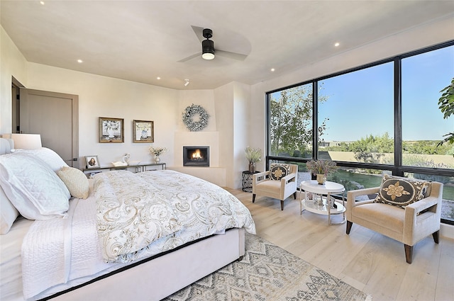 bedroom with wood finished floors, a warm lit fireplace, recessed lighting, and a ceiling fan