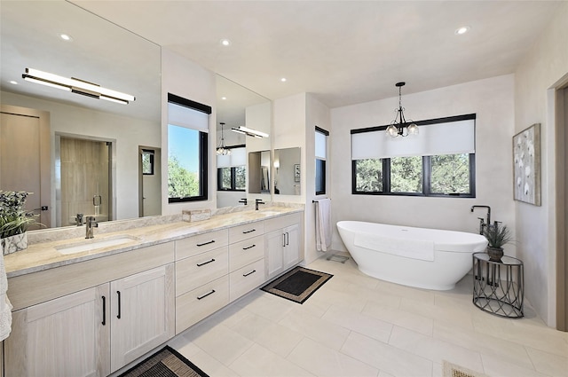bathroom featuring healthy amount of natural light, double vanity, a freestanding tub, a chandelier, and recessed lighting