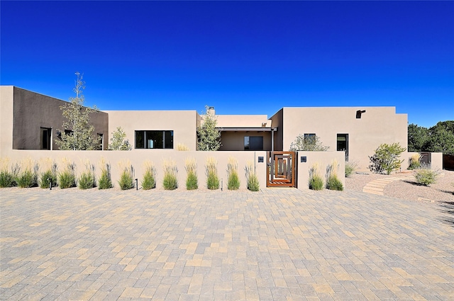pueblo-style house with a gate, fence, and stucco siding