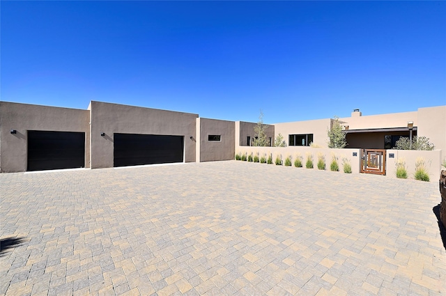 pueblo-style home featuring stucco siding, fence, a garage, and a gate