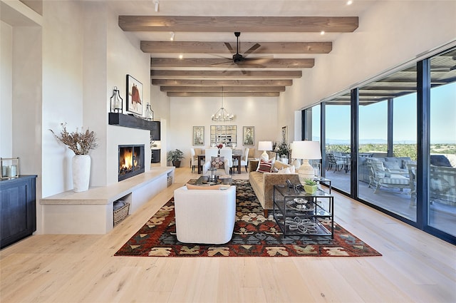 living area featuring a glass covered fireplace, beam ceiling, wood finished floors, a towering ceiling, and a chandelier