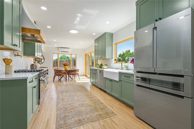 kitchen featuring a wall mounted air conditioner, light wood-type flooring, tasteful backsplash, stainless steel appliances, and green cabinets