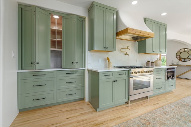 kitchen featuring backsplash, light hardwood / wood-style floors, custom exhaust hood, green cabinetry, and stainless steel stove