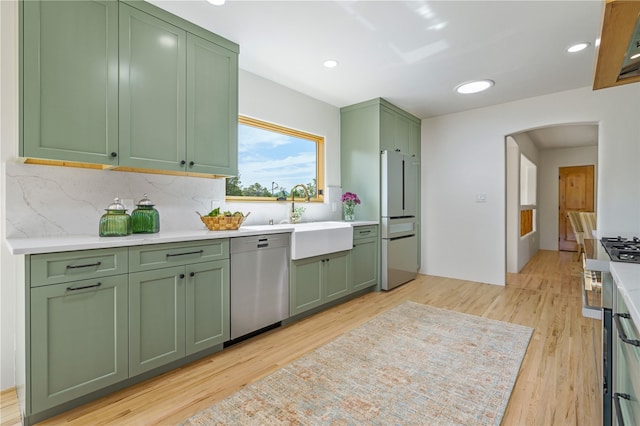 kitchen featuring appliances with stainless steel finishes, backsplash, sink, light hardwood / wood-style flooring, and green cabinets