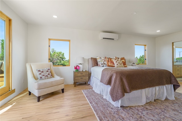 bedroom with multiple windows, connected bathroom, light hardwood / wood-style flooring, and a wall mounted AC