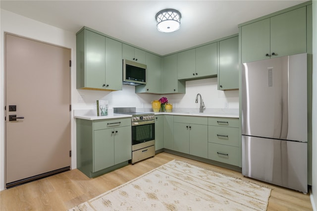 kitchen with green cabinets, sink, stainless steel appliances, and light hardwood / wood-style floors