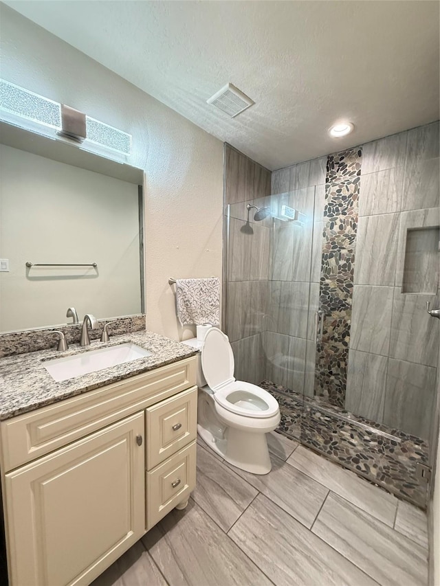 bathroom featuring a tile shower, vanity, a textured ceiling, and toilet